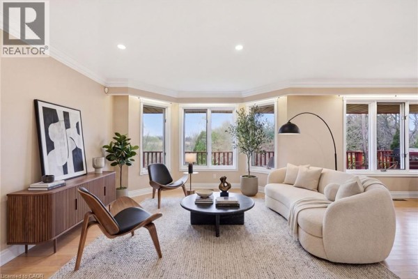 Living room with large bay windows, modern furniture, a curved cream sofa, and wooden floors. - 1610 Concession 7 Road, Hampton