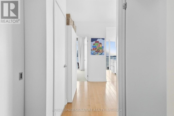Hallway with polished wood floors, white walls, and artwork leading to a bright living area. - 1611 - 1 Market Street, Toronto