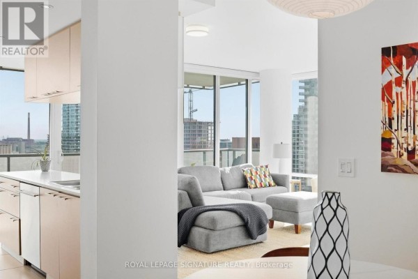 View of the living room from the kitchen area, featuring a grey sectional sofa and floor-to-ceiling windows. - 1611 - 1 Market Street, Toronto