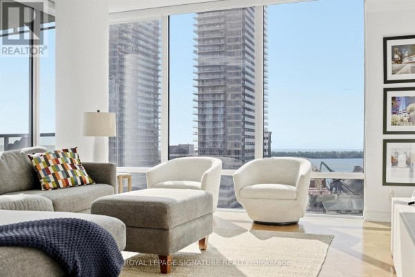 Living room seating area with city skyline and water views through expansive windows. - 1611 - 1 Market Street, Toronto