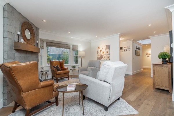 Living room with fireplace, brown leather chairs, grey chairs, bay window, and hallway leading to dining area. - 16114 20 Avenue, Surrey