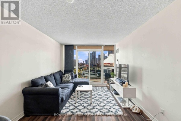 Living room with dark sectional couch, white coffee table, and city view balcony. - 1612 - 25 Lower Simcoe Street, Toronto