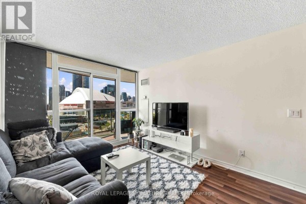 Living room with dark sectional couch, white entertainment unit, and city view balcony. - 1612 - 25 Lower Simcoe Street, Toronto