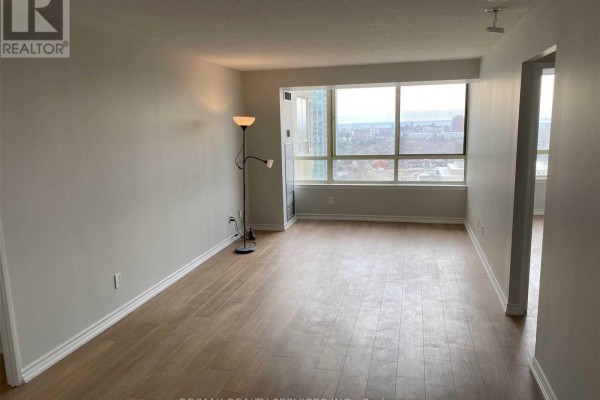 Living room with light wood floors, beige walls, large window with city view, and floor lamp. - 1612 - 3605 Kariya Drive, Mississauga