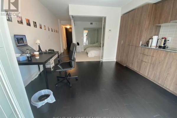 Apartment with black floors, desk with laptop, and open doorway to bedroom. - 1612 - 955 Bay Street, Toronto