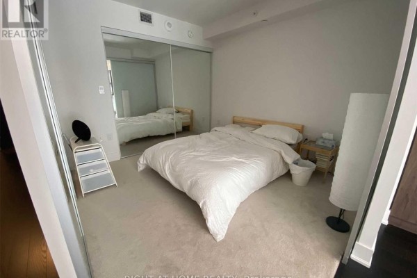 Bedroom with queen-size bed, mirrored closet doors, and carpeted floor. - 1612 - 955 Bay Street, Toronto