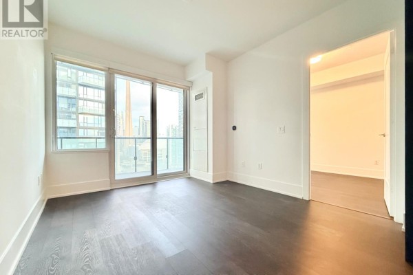 Bedroom with dark wood floors, white walls, sliding glass doors, and doorway to hallway. - 1613 - 480 Front Street W, Toronto