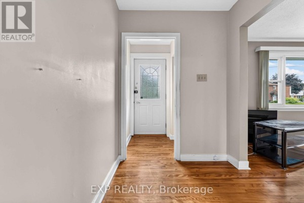Interior view of a hallway with hardwood floors leading to a glass-paned front door. - 1613 Queensdale Avenue, Ottawa