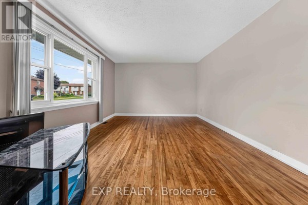 Empty living room with hardwood floors and a large bay window overlooking the street. - 1613 Queensdale Avenue, Ottawa