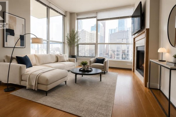 A bright living room with a sectional sofa, fireplace, and large windows with city views. - 1615, 222 Riverfront Avenue Sw, Calgary