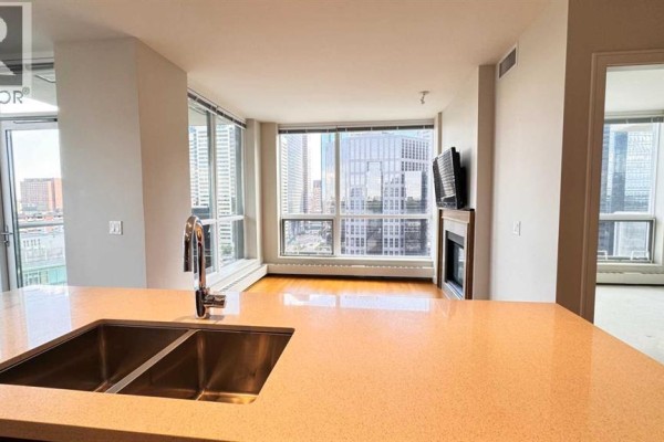 A kitchen island with a sink overlooking a living area with large windows and city views. - 1615, 222 Riverfront Avenue Sw, Calgary