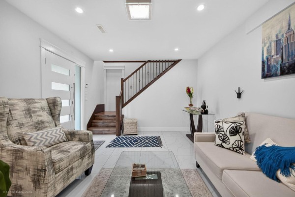 Living room with a white sofa, patterned armchair, wood stairs, and glass console table. - 16166 92 Avenue, Surrey