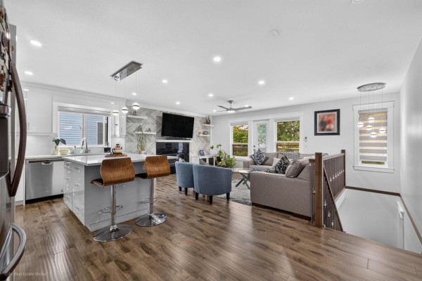 Open-concept kitchen and living area with a light grey island, stainless steel appliances, and fireplace. - 16166 92 Avenue, Surrey