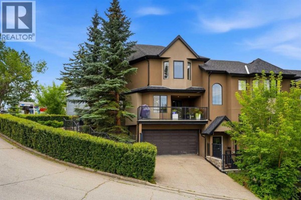 A multi-level townhouse complex with a sloped driveway, garage, and balcony, set against a backdrop of trees. - 1619 24 Avenue Sw, Calgary