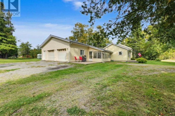 Side view of a light yellow house with a three-car garage and a covered patio. - 1619 Centreville Road, Stone Mills