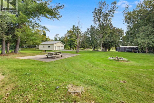 View of a large green lawn with a concrete pad, picnic table, and wooded area. - 1619 Centreville Road, Stone Mills