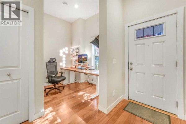 Entryway of a townhouse with hardwood floors, a white door, and an office space with a desk and chair. - 162, 2802 Kings Heights Gate Se, Airdrie