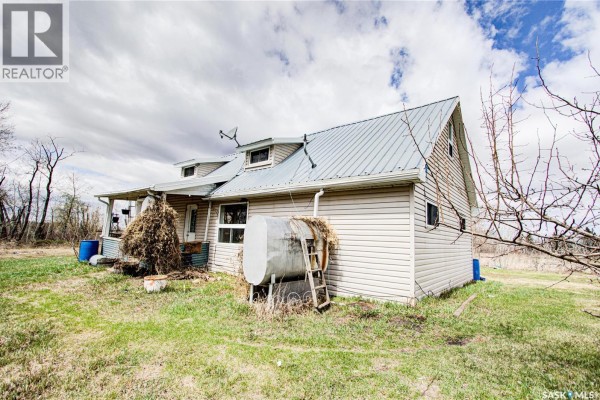 Side view of a beige vinyl-sided house with a metal roof, including a covered porch and water tank. - 162 Acres Farmland East Of Debden, Canwood Rm No  494