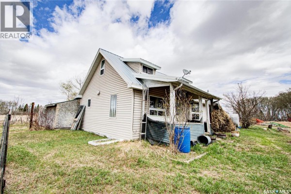 Corner view of a beige vinyl-sided house with a metal roof, showing a porch and surrounding grassy area. - 162 Acres Farmland East Of Debden, Canwood Rm No  494