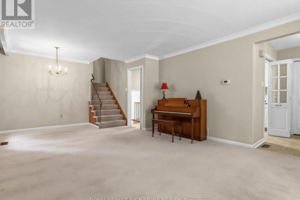 Living room with beige carpet, a staircase, a piano, and a doorway to the kitchen. - 162 Bathgate Drive, Toronto