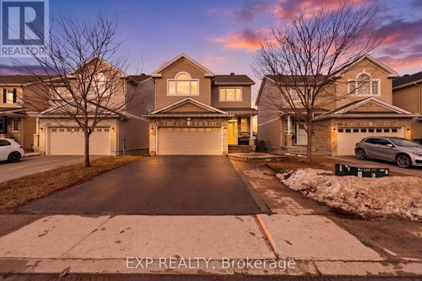 Exterior view of a beige townhouse with a double garage and asphalt driveway under a colorful sunset sky. - 162 Bert Hall Street, Arnprior