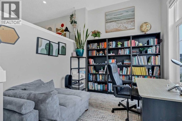 A cozy office space with a sectional sofa, built-in bookshelf, and wall art. - 162 Chinook Gate Boulevard Sw, Airdrie
