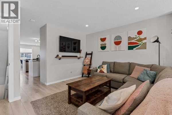 Living room with sectional sofa, coffee table, wall-mounted TV, and view of kitchen. - 162 Chinook Gate Boulevard Sw, Airdrie
