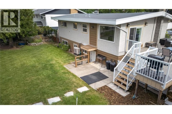 Backyard with a grassy lawn, concrete patio, and wooden deck with stairs. - 162 Woodlands Place, Penticton