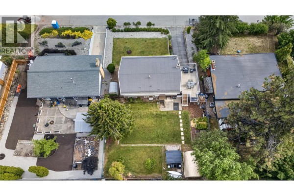 Aerial view of a property with a backyard, deck, and surrounding houses. - 162 Woodlands Place, Penticton