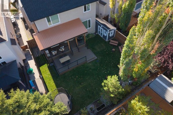 Aerial view of a backyard with a covered deck, green grass, a trampoline, and a small blue shed. - 1621 Strathcona Drive Sw, Calgary