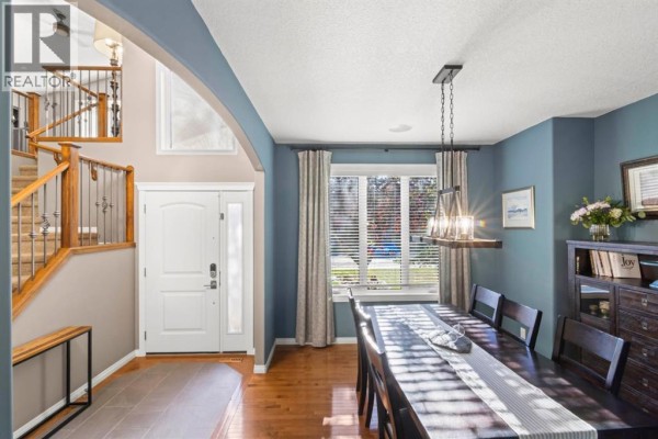 Formal dining room with a dark wood table, chairs, large window with blinds, and a contemporary chandelier. - 1621 Strathcona Drive Sw, Calgary