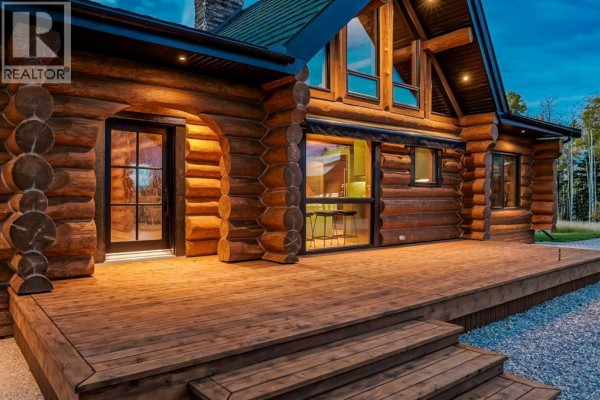 Close-up of the wooden deck and log exterior of the house with glass doors. - 162104 376 Street W, Rural Foothills County