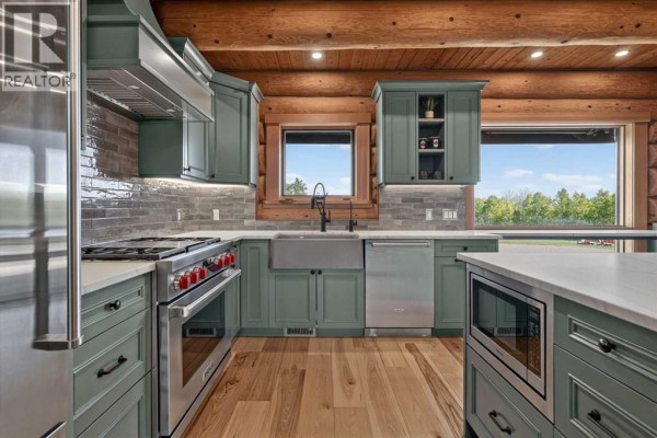 Kitchen featuring green cabinets, stainless steel appliances, a farmhouse sink, and large windows. - 162104 376 Street W, Rural Foothills County
