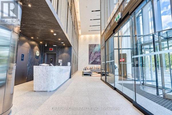 View of the apartment lobby from the side, showing a reception desk, seating area, and revolving doors. - 1622 - 585 Bloor Street E, Toronto