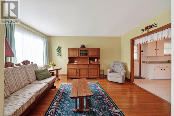 Living room with light yellow walls, a beige striped sofa, a wooden hutch, and a green patterned rug. - 1624 Aubin Avenue, Cornwall