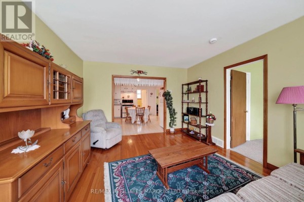 Living room with light yellow walls, a beige armchair, a wooden hutch, and a view into the kitchen and hallway. - 1624 Aubin Avenue, Cornwall
