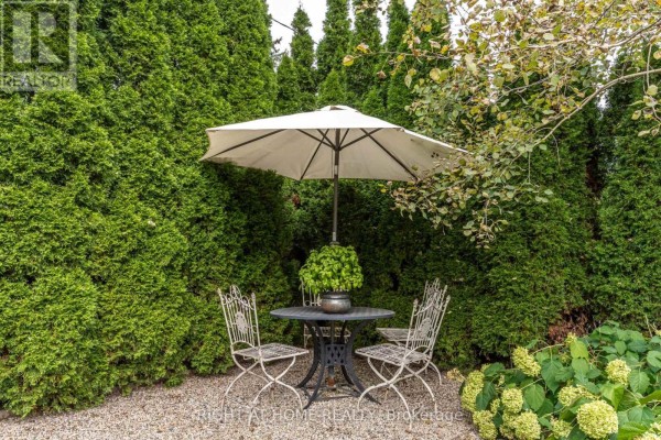 Outdoor seating area with a table, umbrella, and chairs surrounded by lush green hedges. - 1627 Rometown Drive, Mississauga