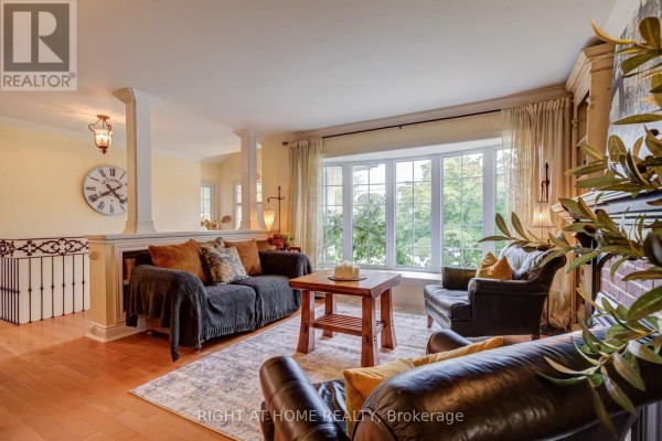 Living room with sofas, armchairs, a coffee table, fireplace, and bay window with garden view. - 1627 Rometown Drive, Mississauga