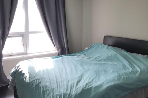 Bedroom with a queen bed covered in a light blue comforter and a large window with grey curtains. - 1628 - 500 Doris Avenue, Toronto