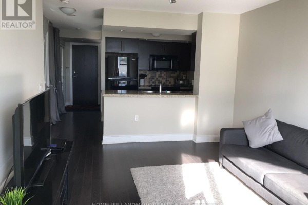 Living room with a sofa and television, opening to a dark wood kitchen with black appliances and granite countertops. - 1628 - 500 Doris Avenue, Toronto