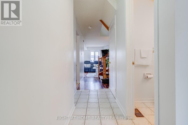 Interior hallway with white walls, tiled floor, wood flooring at the end, and a wooden staircase. - 163 - 302 College Avenue W, Guelph