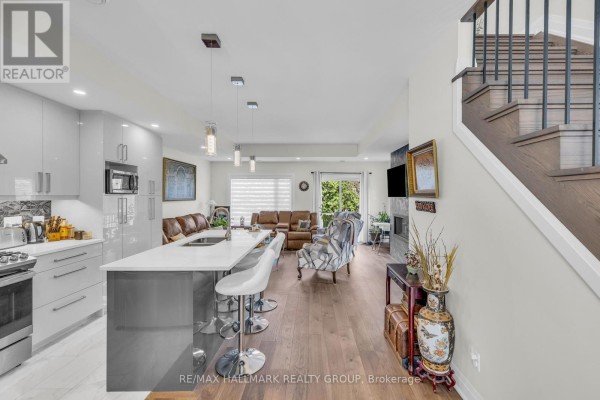 Open concept kitchen with grey island, stainless steel appliances, and living room with fireplace and furniture. - 163 Longpre Street, Ottawa