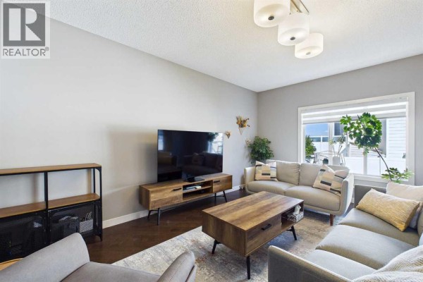 Living room with a sectional sofa, coffee table, entertainment unit, and television, with natural light from a large window. - 163 Panamount Circle Nw, Calgary