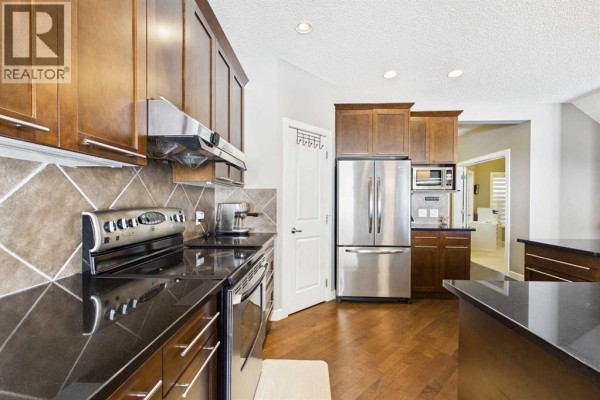 Kitchen featuring dark wood cabinets, granite countertops, stainless steel appliances, and a diagonal tile backsplash. - 163 Panamount Circle Nw, Calgary
