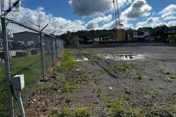 Chain-link fence with barbed wire along the perimeter of a gravel lot with patchy grass and puddles. - 163 Ram Forest Road, Whitchurch Stouffville