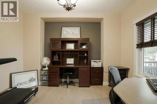 Home office with a large wooden desk, treadmill, and window blinds. - 163 Rattlepan Creek Crescent, Fort Mcmurray