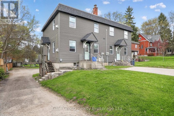 Side view of the grey duplex showing a grassy yard, concrete steps, and driveway. - 163 Thames Street N, Ingersoll