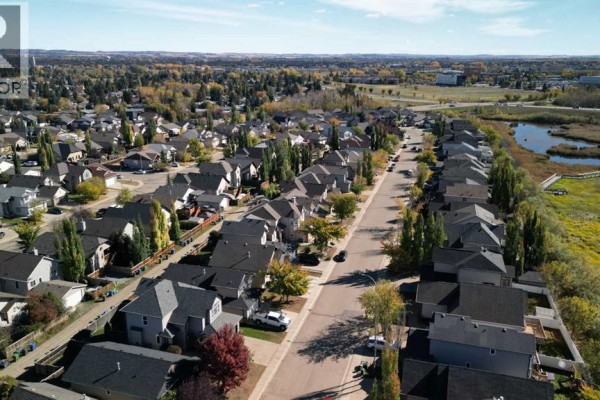 Aerial view of a residential street in Red Deer with houses and a pond on the right. - 163 Wiley Crescent, Red Deer