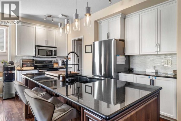 Modern kitchen with white cabinets, stainless steel appliances, a large island with a sink, and granite countertops. - 163 Wiley Crescent, Red Deer
