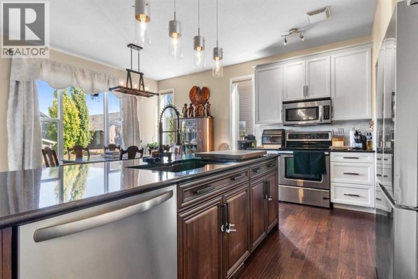 Kitchen and dining area with a large island, dark wood cabinets, and a view of the backyard and trees. - 163 Wiley Crescent, Red Deer